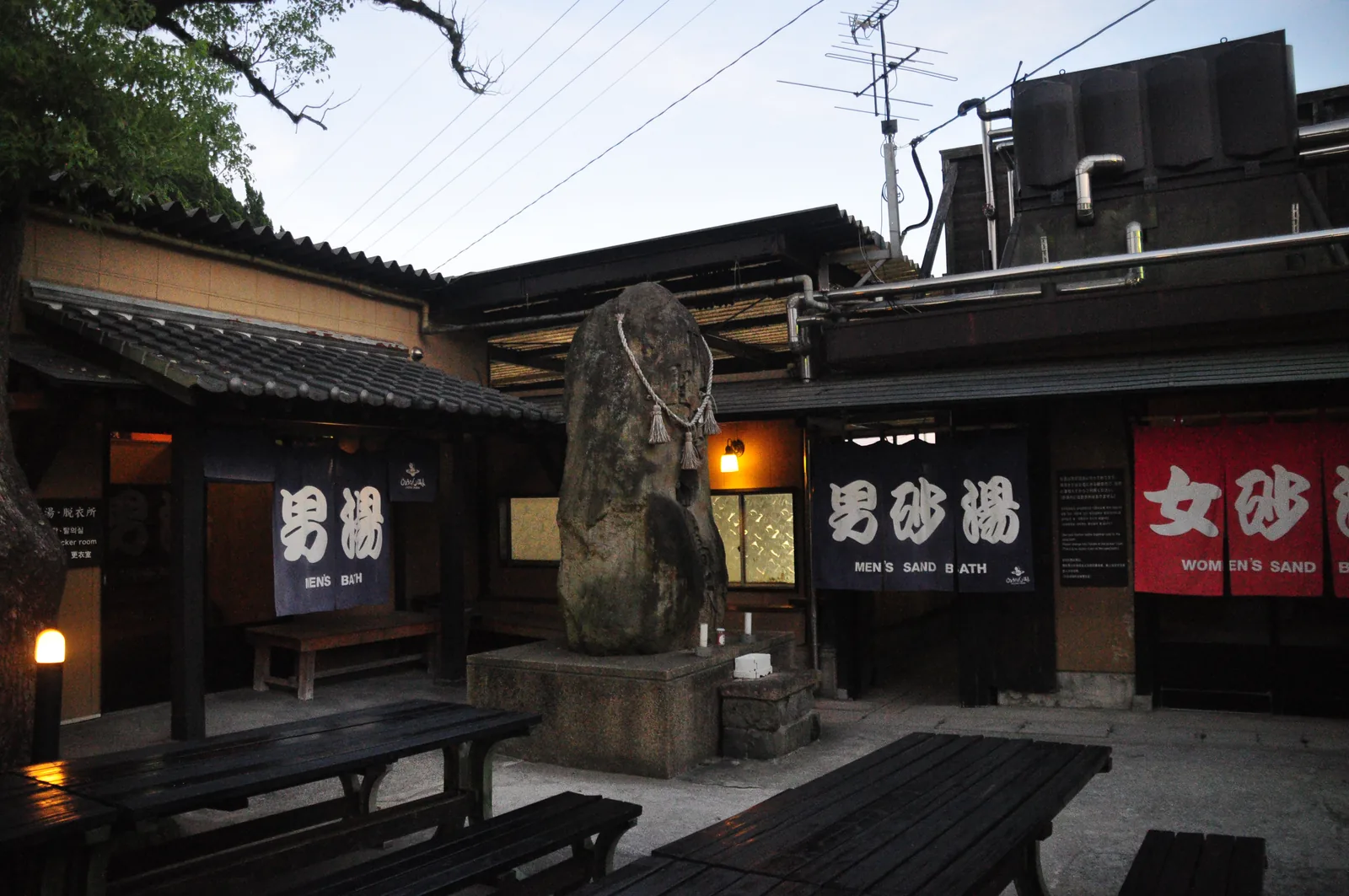 葫蘆溫泉中庭的高大立石，左邊是「男湯」暖簾，右邊是「男砂湯」暖簾與紅色的「女砂湯」暖簾