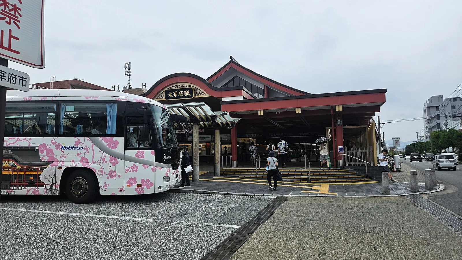 Nishitetsu Dazaifu Station with its red roof, a bus painted with plum blossom parked in front