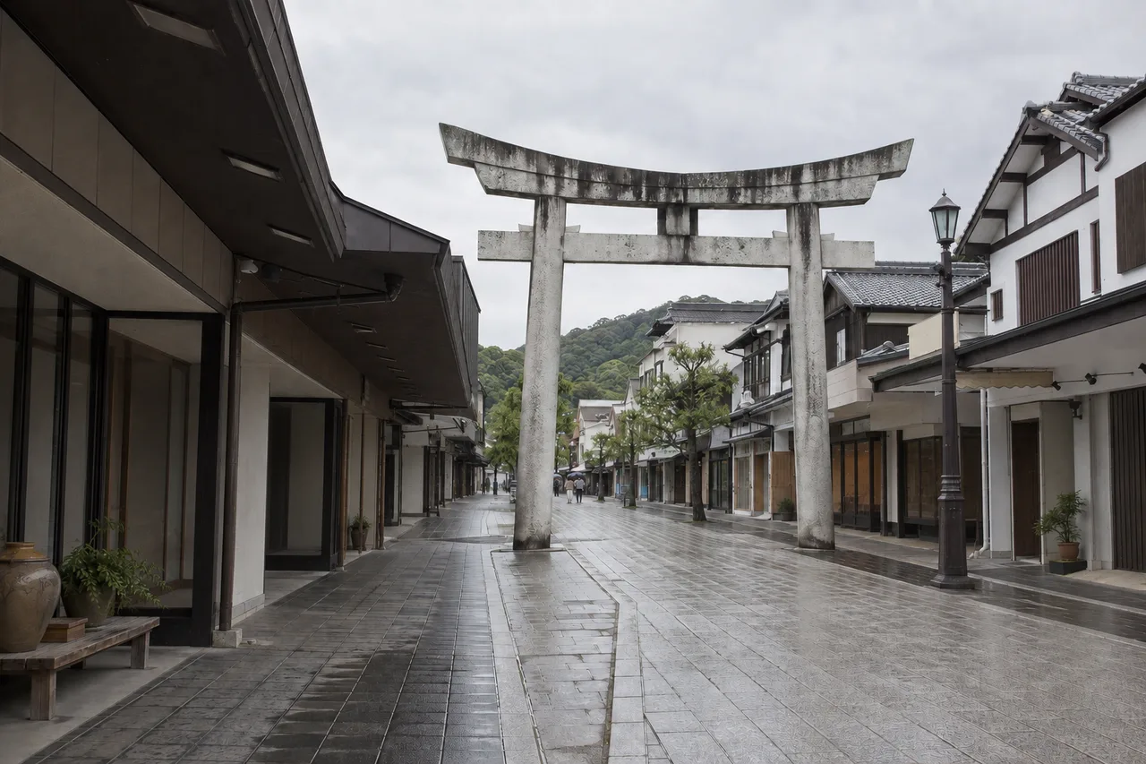 橫跨參道的灰色石造鳥居全景,兩旁是低矮屋簷的商店
