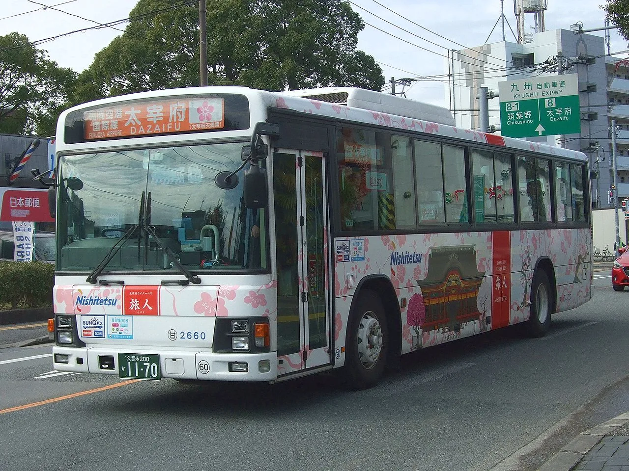 A white Nishitetsu bus decorated with plum and cherry blossom, its front sign showing Dazaifu