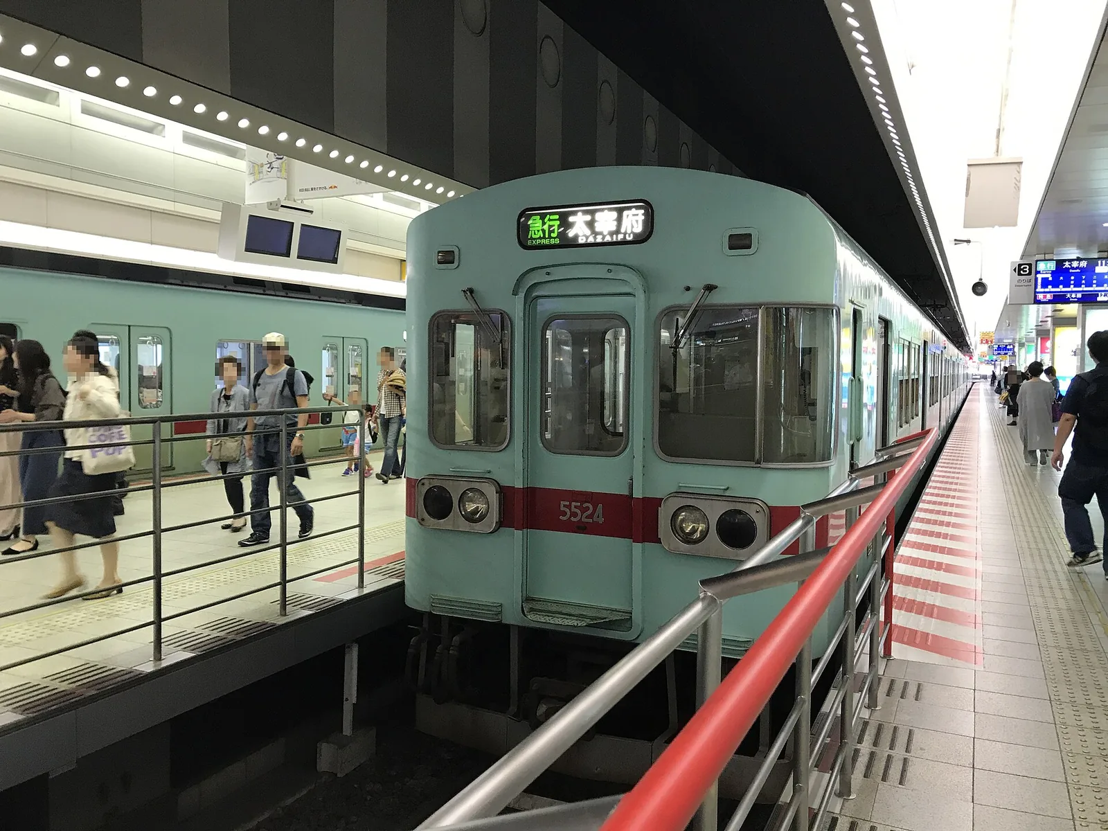 A pale green Nishitetsu train at a platform, its destination board reading Express for Dazaifu