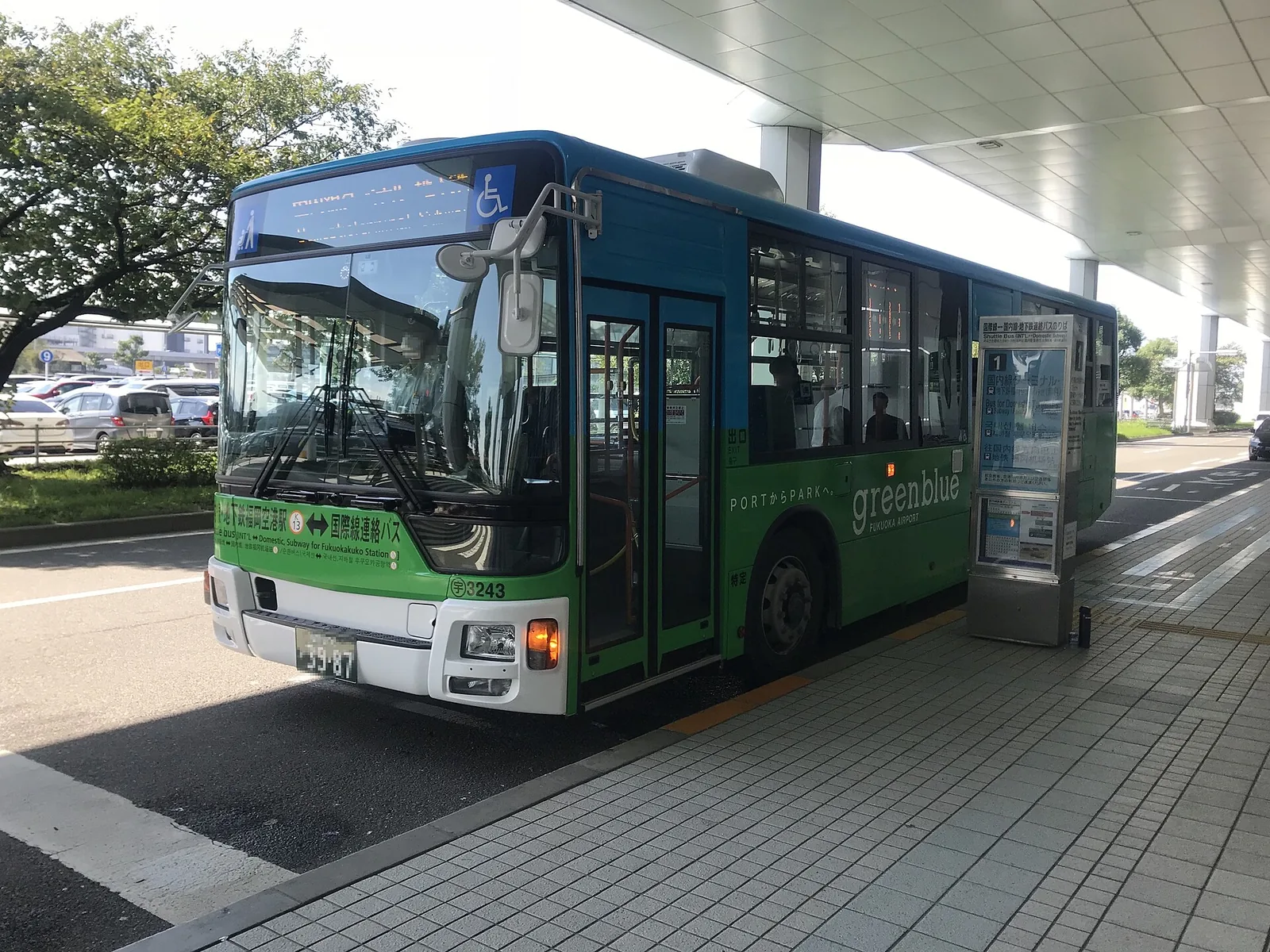 A green and blue Fukuoka Airport shuttle bus parked at a covered stop