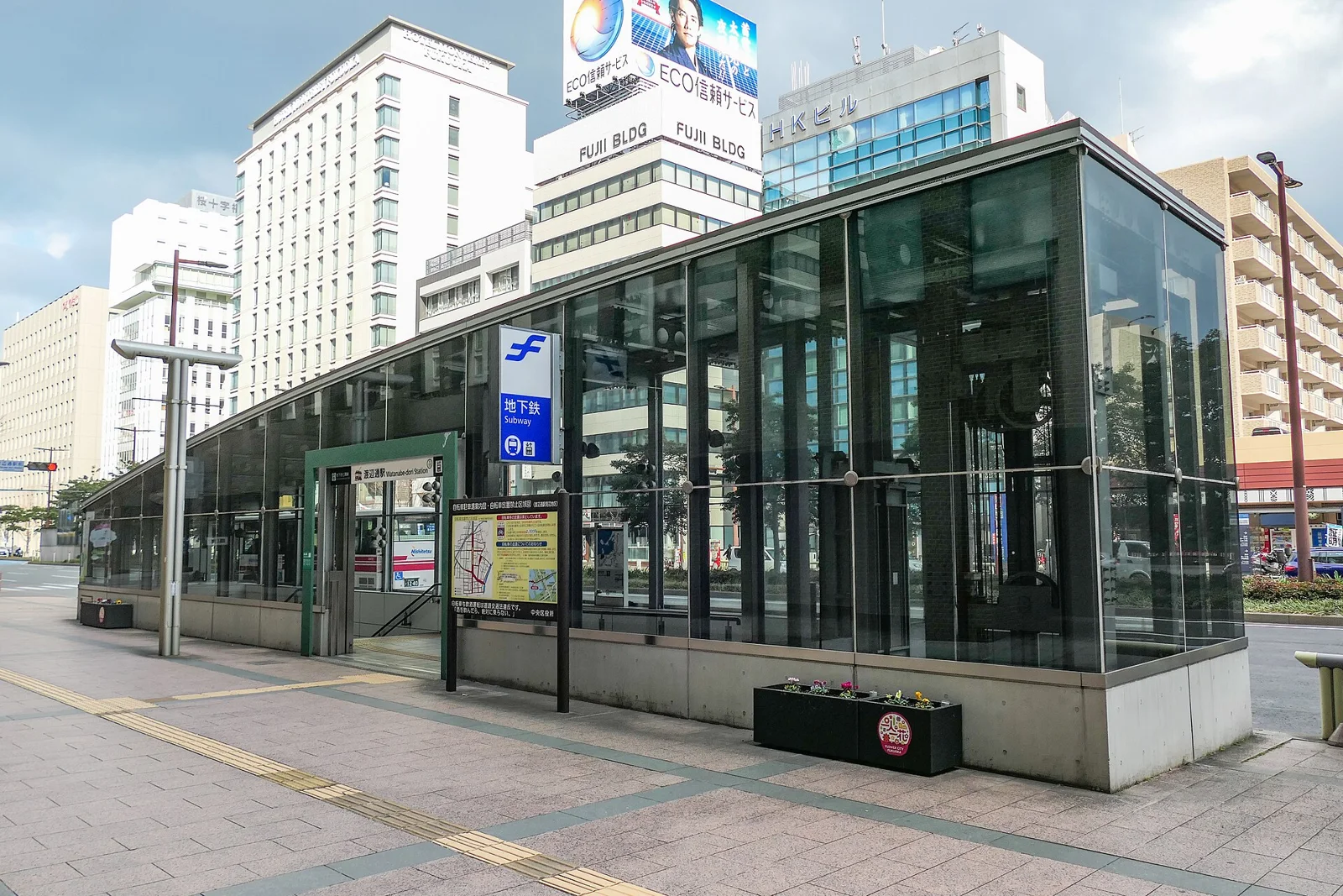 The glass-walled Exit 1 of Watanabe-dori Station with a subway sign, office buildings behind