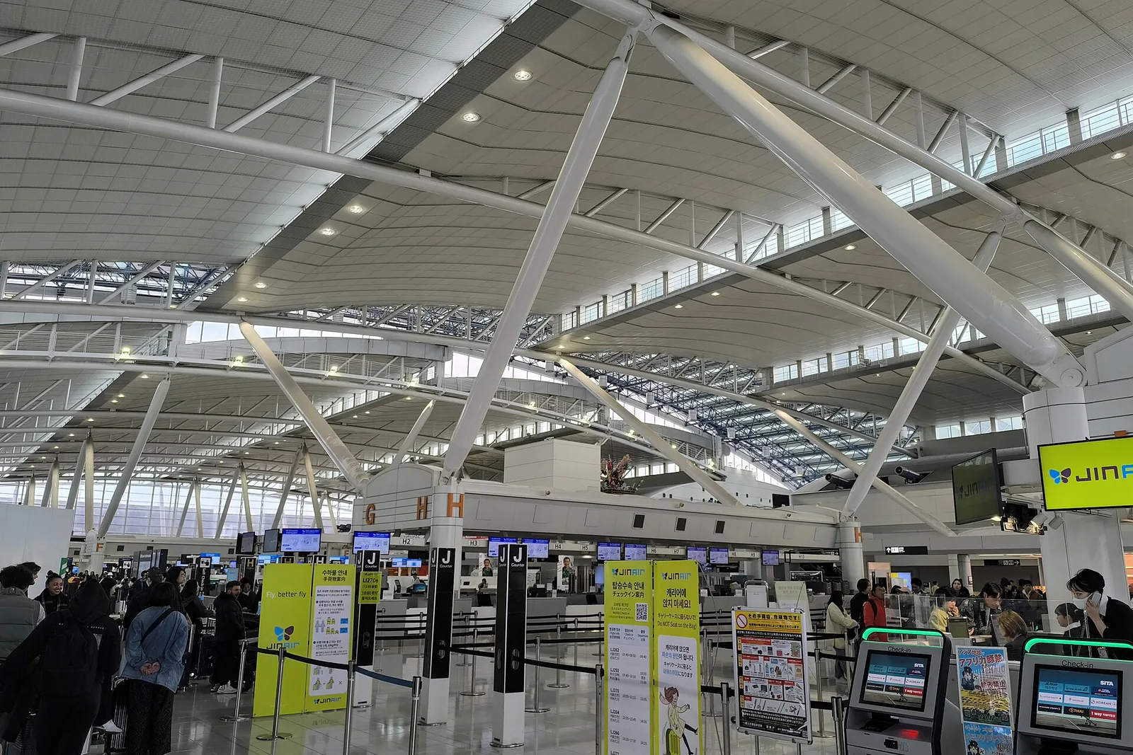 Fukuoka Airport's international departures hall under a high steel-truss roof, with check-in counters and queues