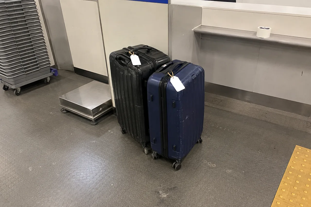 Two tagged suitcases beside a baggage scale and delivery counter