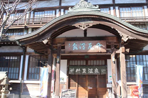The curved karahafu gable over the entrance of Takegawara Onsen, with a name board reading 竹瓦温泉 and a noren curtain over the doors