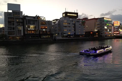 The Naka River at dusk, a lit-up water bus passing in front of riverside buildings