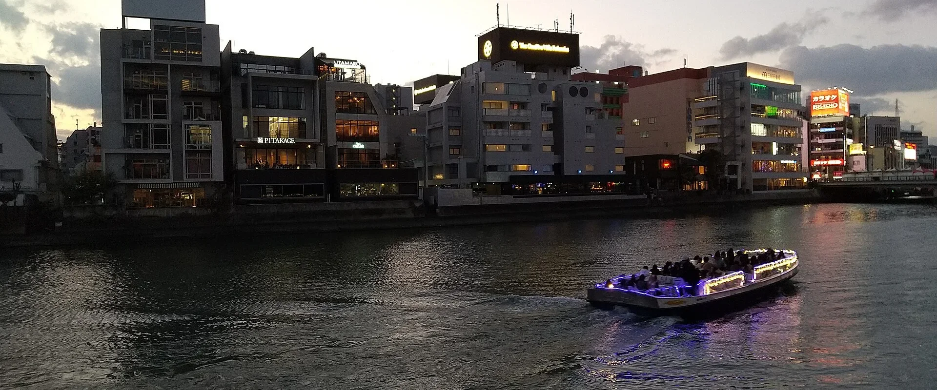The Naka River at dusk, a lit-up water bus passing in front of riverside buildings
