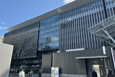 Hakata Station's glass front on a sunny day, with people walking across the plaza