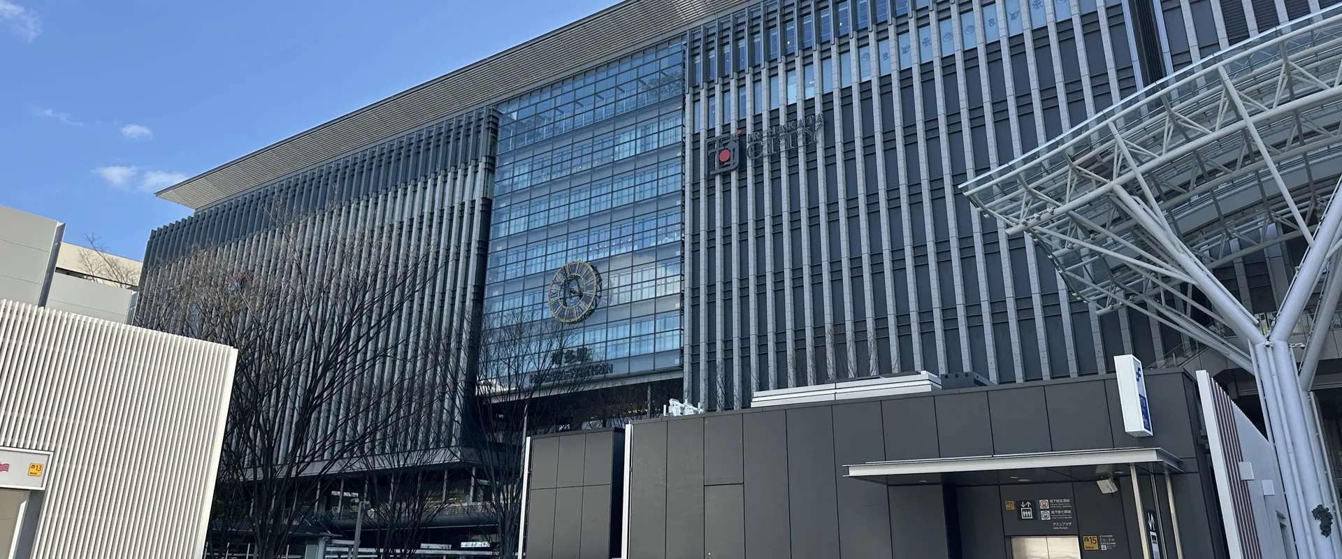 Hakata Station's glass front on a sunny day, with people walking across the plaza