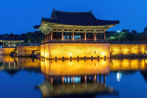 A lit Donggung pavilion reflected in Wolji Pond under a deep blue evening sky