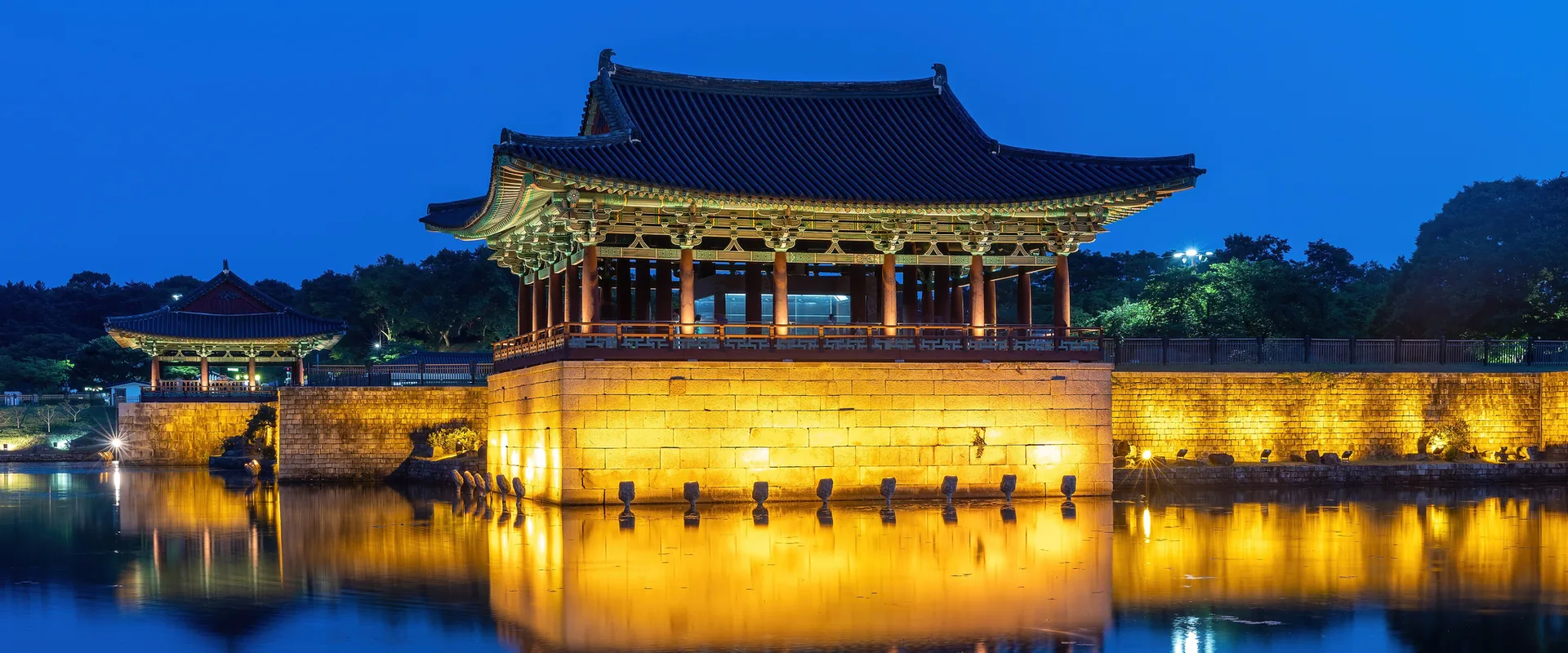 A lit Donggung pavilion reflected in Wolji Pond under a deep blue evening sky