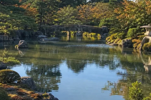 Garden pond, stone bridge and pines in autumn light