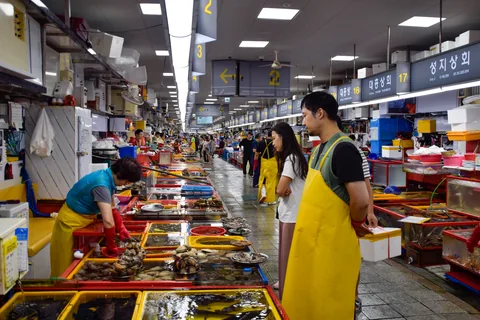 An aisle of seafood stalls with live tanks and vendors in aprons at Jagalchi Market, Busan