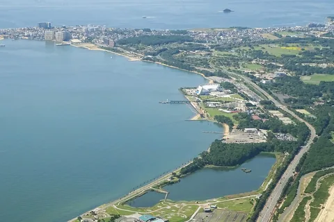 Uminonakamichi from the air: Marine World's white building and its pier on the bay shore, with the park's woods and lawns running to the town at the end of the sandbar