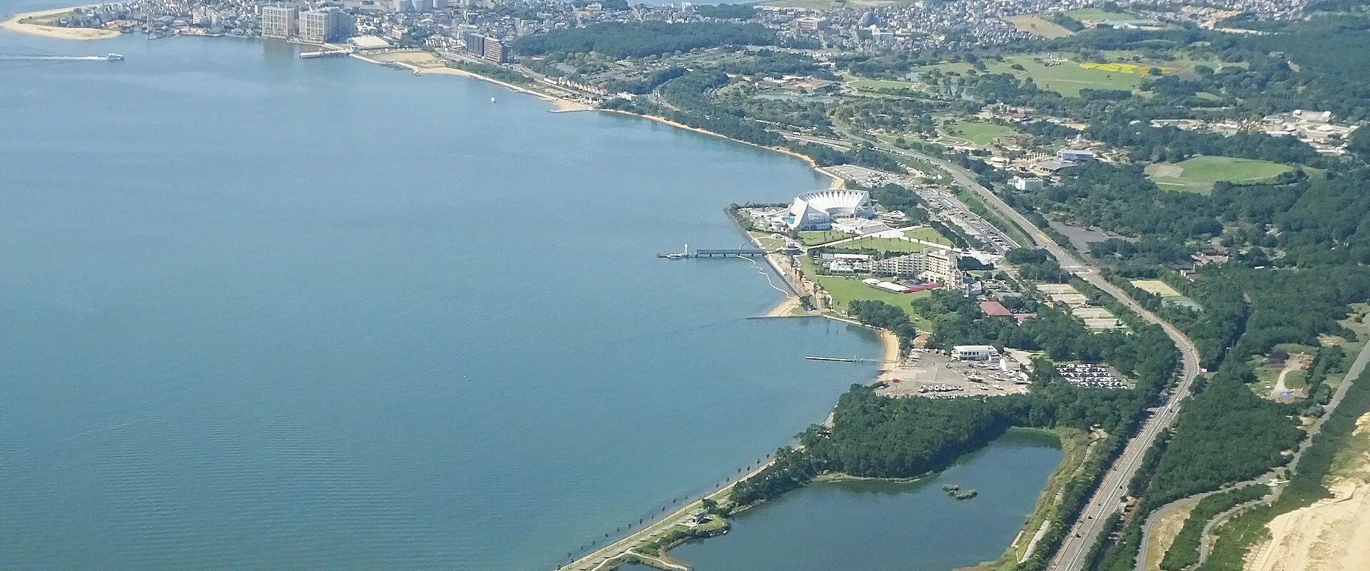 Uminonakamichi from the air: Marine World's white building and its pier on the bay shore, with the park's woods and lawns running to the town at the end of the sandbar