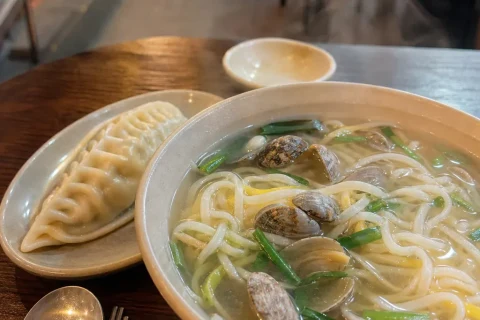 A steaming bowl of clam knife-cut noodle soup with a dumpling