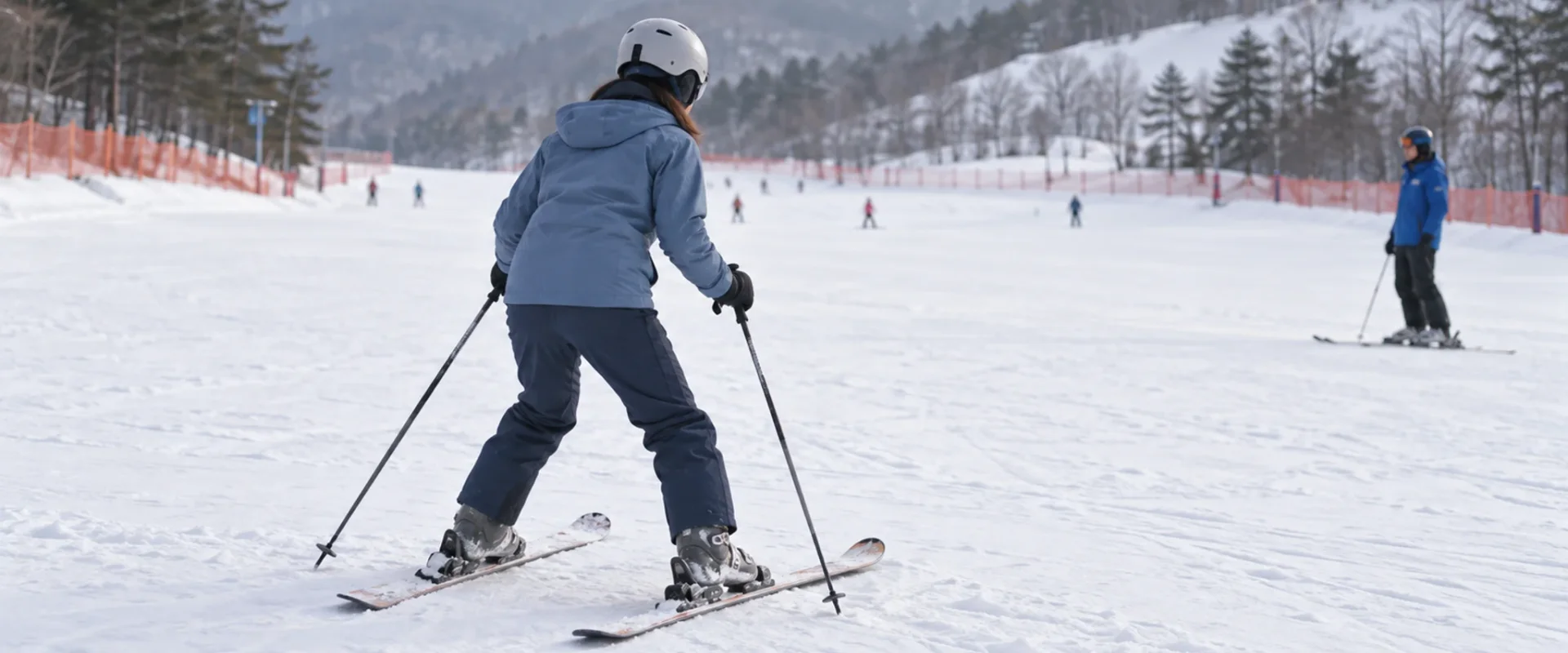 An adult skier with a helmet and ski poles on a gentle practice slope