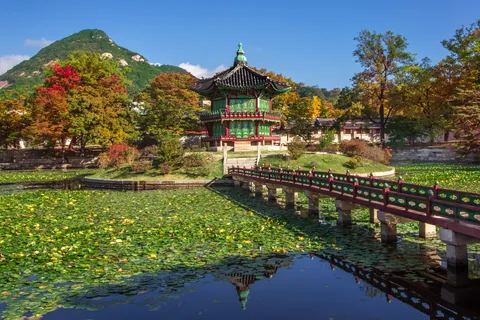 Hyangwonjeong Pavilion on its island in Gyeongbokgung, with a wooden bridge, red and orange trees and Bugaksan behind