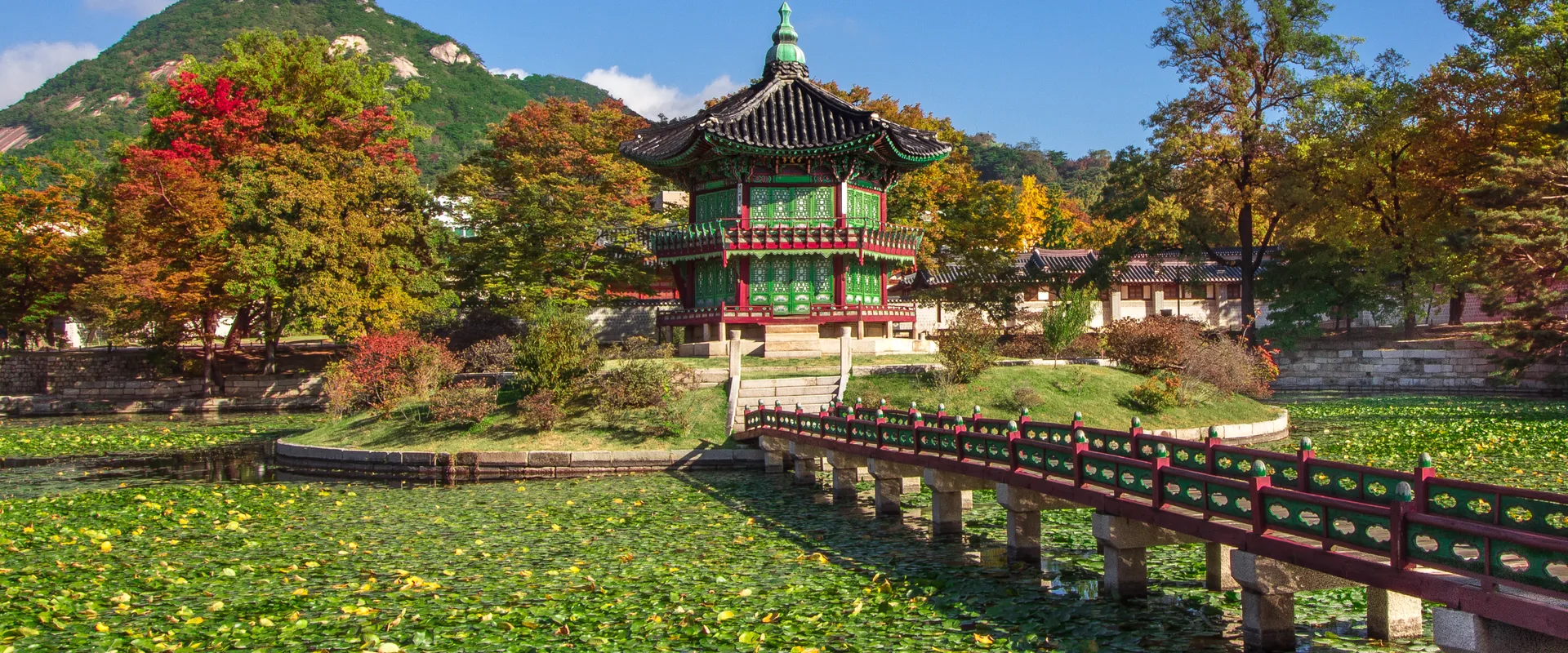 Hyangwonjeong Pavilion on its island in Gyeongbokgung, with a wooden bridge, red and orange trees and Bugaksan behind