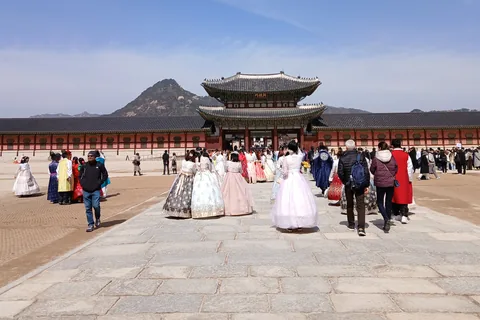 Visitors in hanbok walk up a wide stone path towards Heungnyemun Gate, with Bugaksan mountain behind it