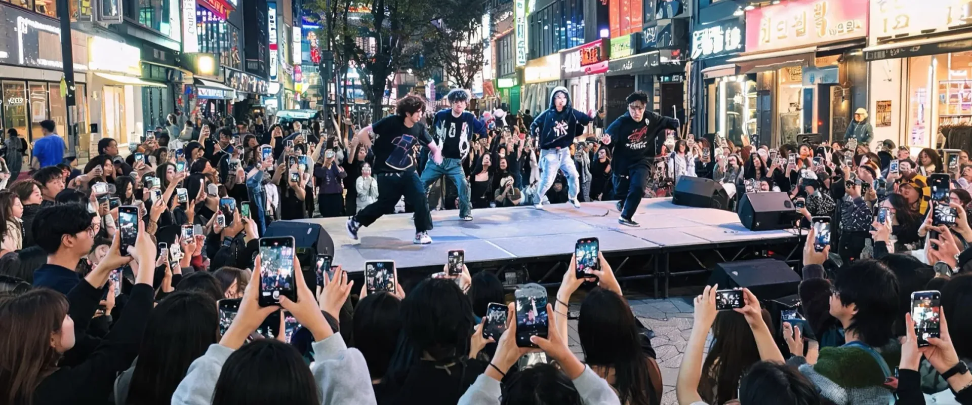 A crowd watching an outdoor performance under shop lights