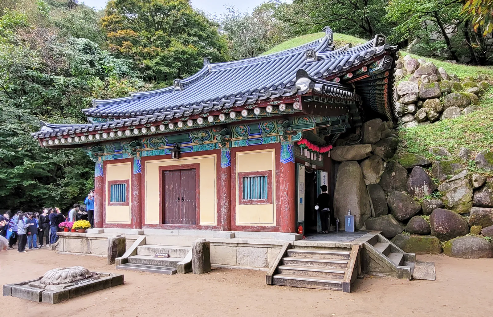 The tiled hall in front of Seokguram Grotto, set against a rocky, grassy mound, with a group of visitors to the left