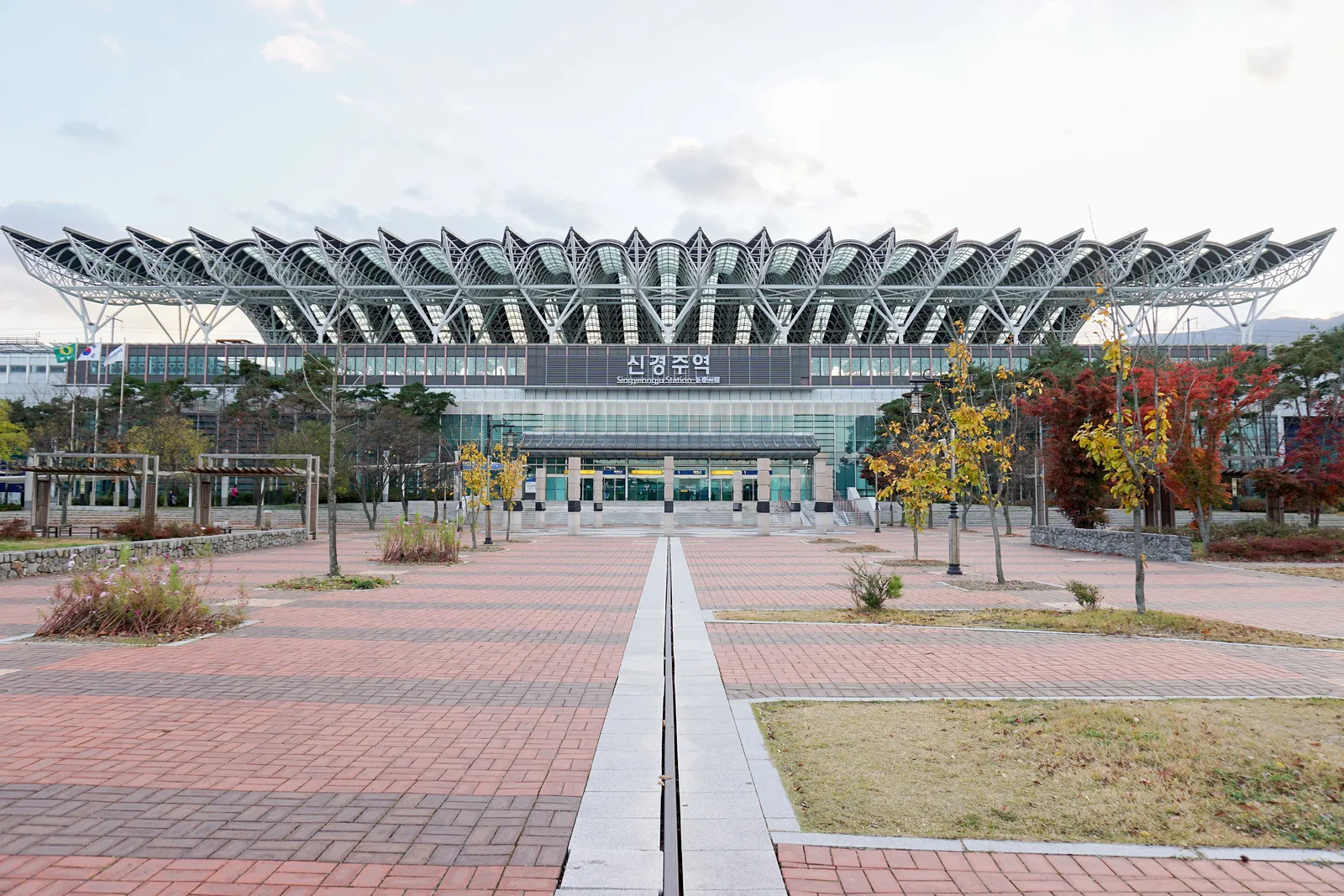 The steel-roofed Gyeongju Station building at the end of a wide plaza, still signed Singyeongju