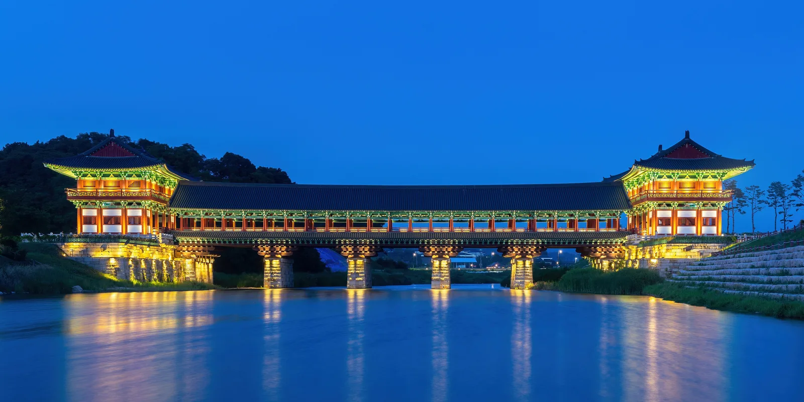 Woljeonggyo Bridge lit up under a blue evening sky, reflected in the river