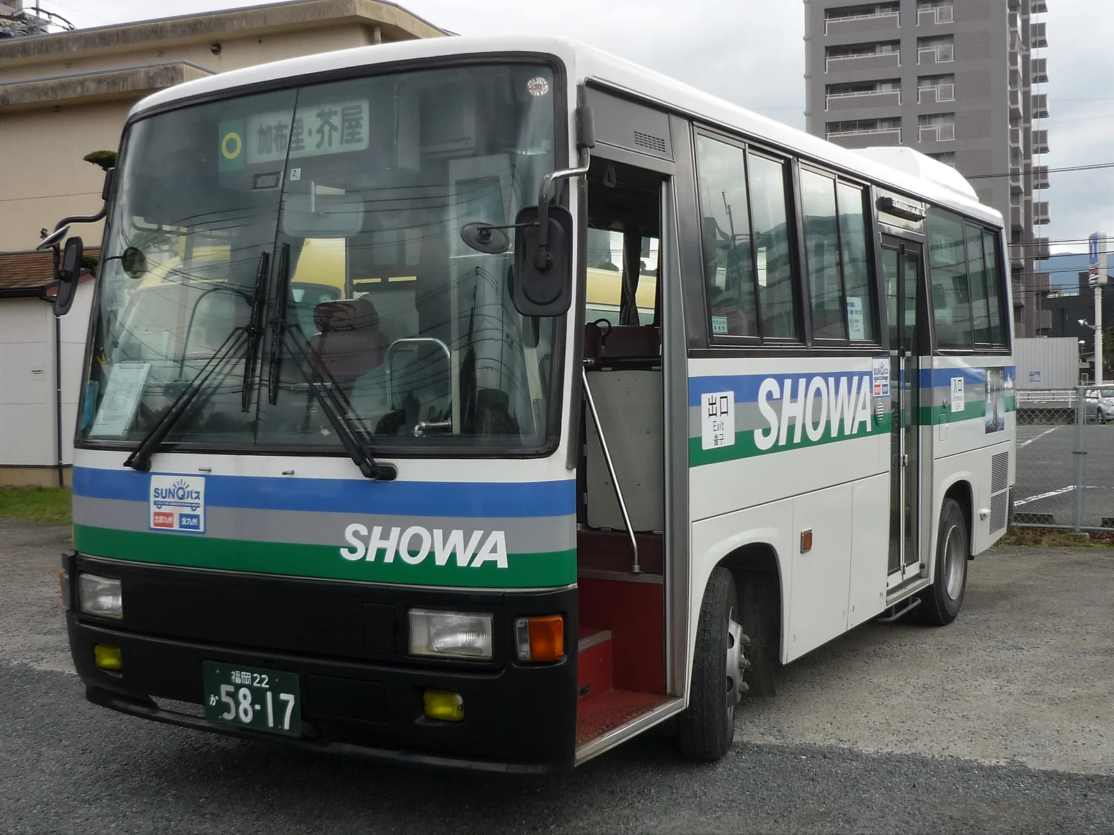 A white Showa Bus with blue and green stripes parked near a stop in Itoshima, its destination sign above the windshield