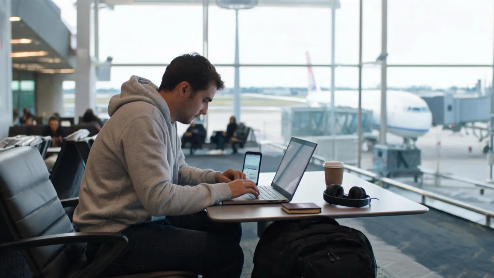 A traveler using a laptop and smartphone in an airport lounge