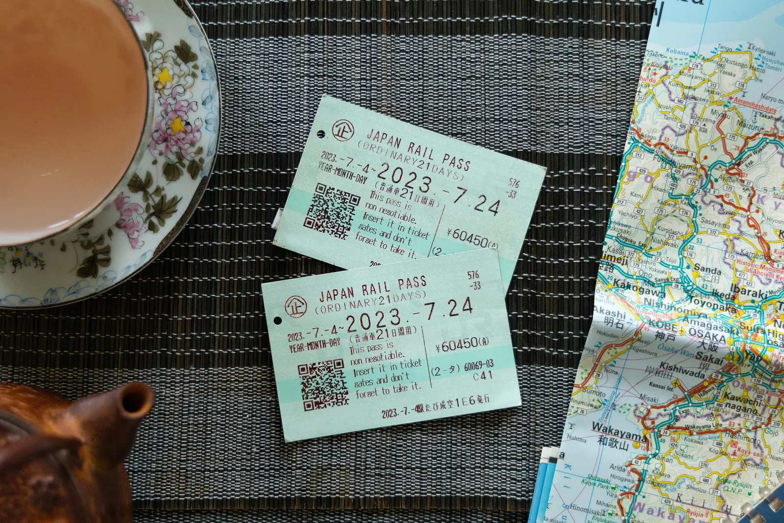 Two Japan Rail Pass tickets on a table next to a teacup and a folded map
