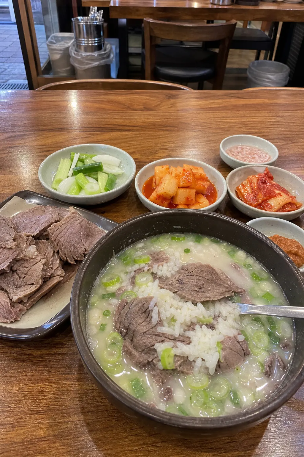 A bowl of gomtang with sliced beef and side dishes