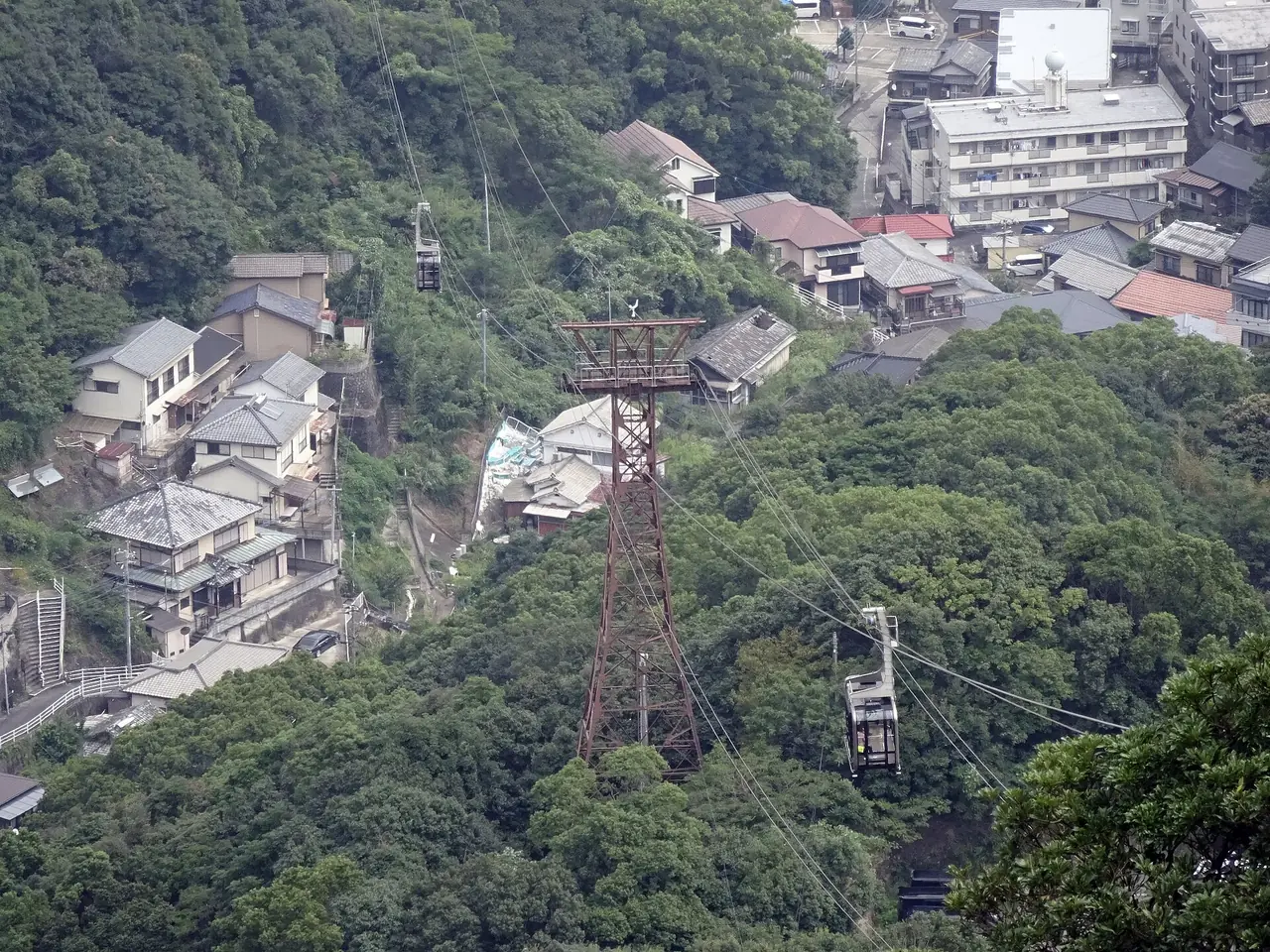 A Mount Inasa ropeway car and a steel pylon on the cables above a wooded hillside