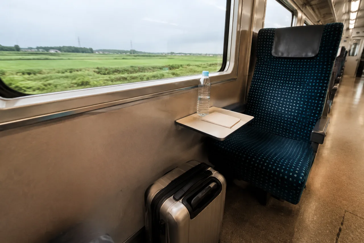 A train window seat with a small table and a suitcase in the footwell