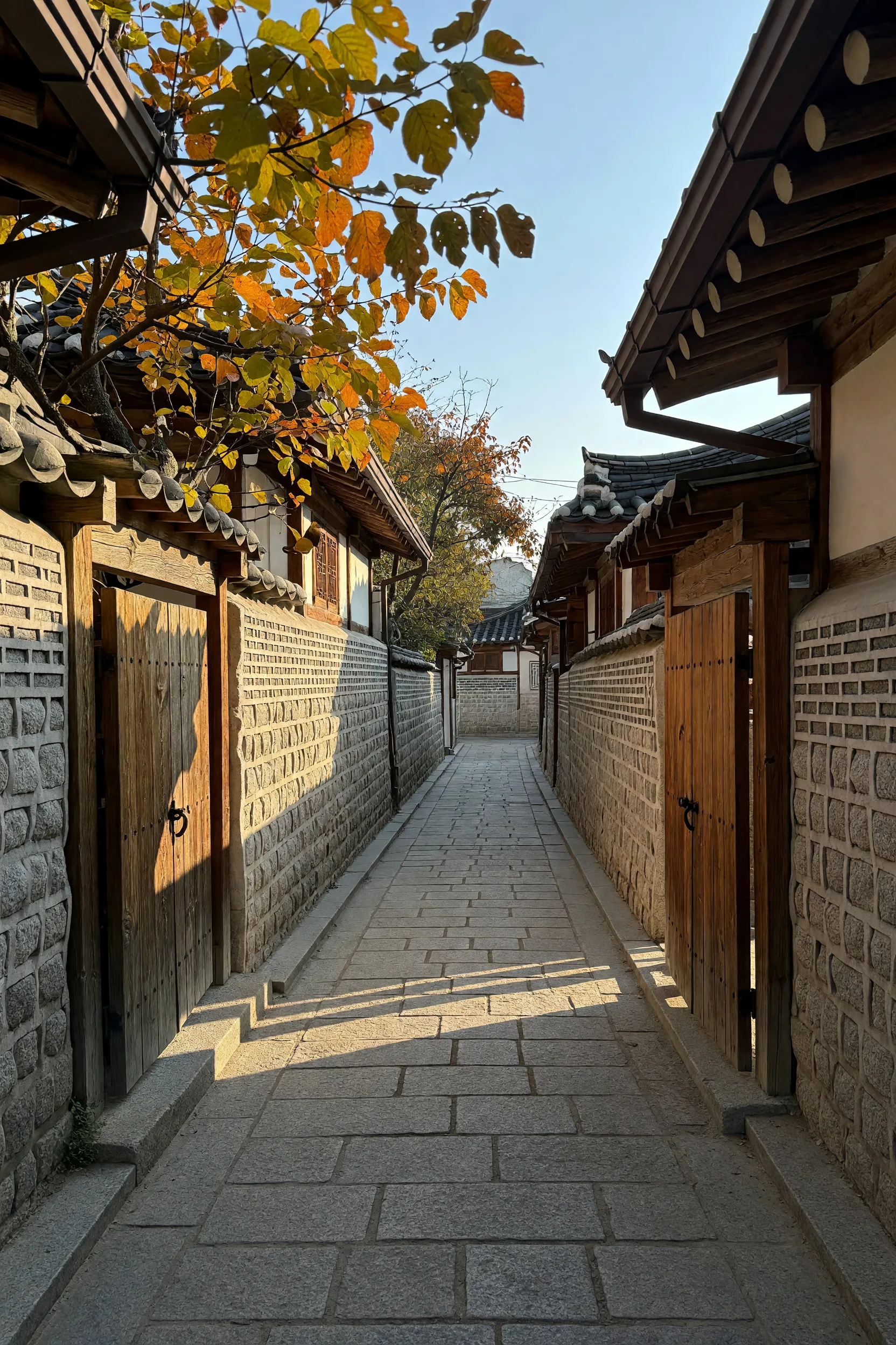 An empty stone-walled alley seen from its entrance, wooden gate doors closed along both sides.