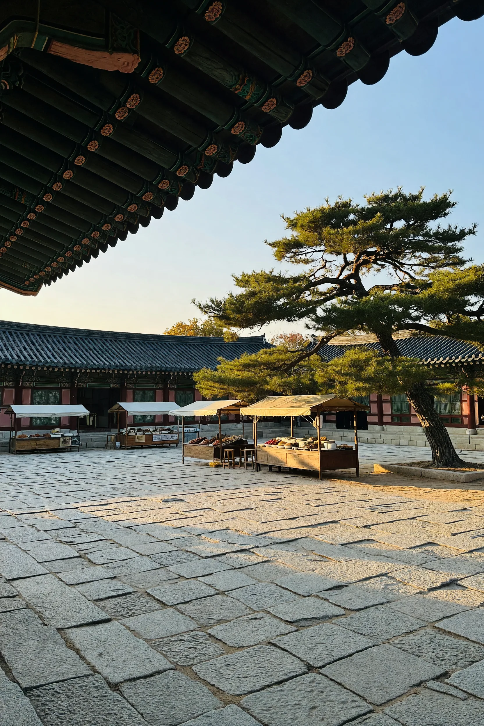 A long tiled roof of a royal palace precinct in early autumn, with a paved courtyard in front.