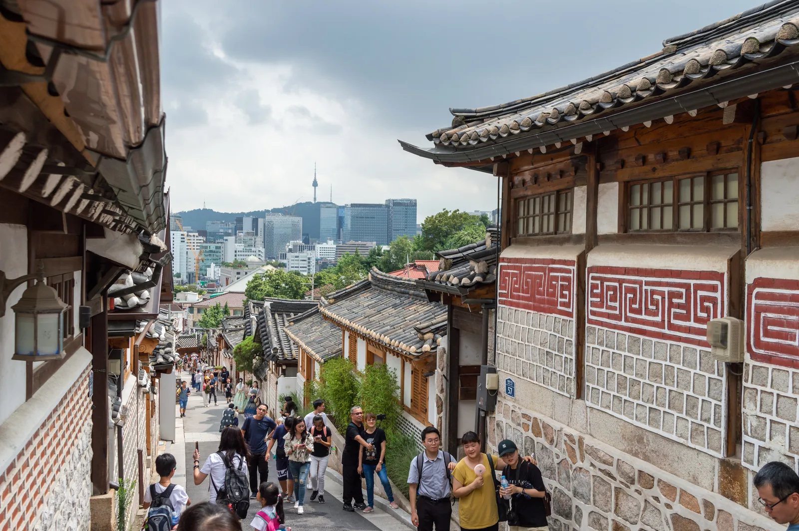 Visitors walking down a sloping lane between tiled hanok houses, with N Seoul Tower on the skyline