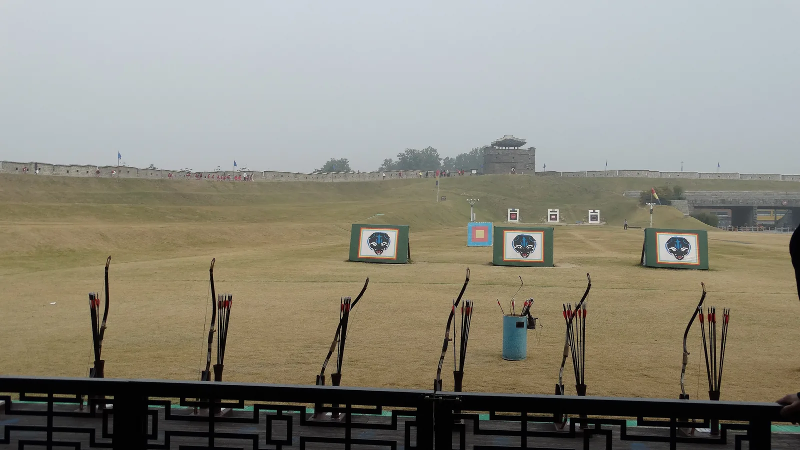 Traditional bows standing in a rack behind a railing at Yeonmudae, with targets at the far end of a grass field