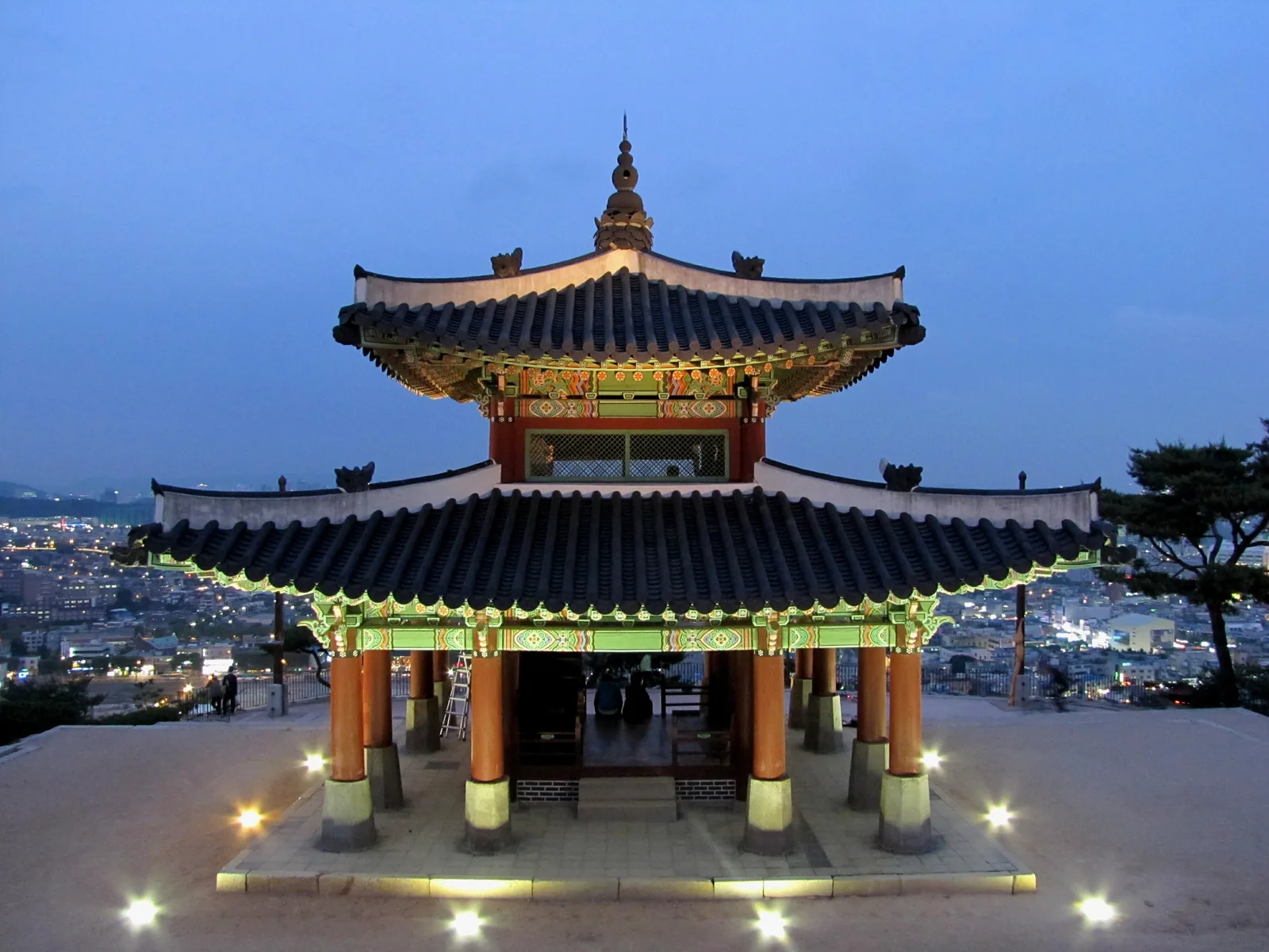 The two-storey Seojangdae pavilion lit up at dusk, with the lights of Suwon spread out below the hilltop