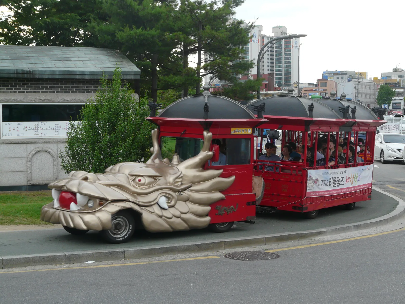 The Hwaseong Trolley on a road: a dragon-head tractor pulling red carriages with black roofs and passengers on board