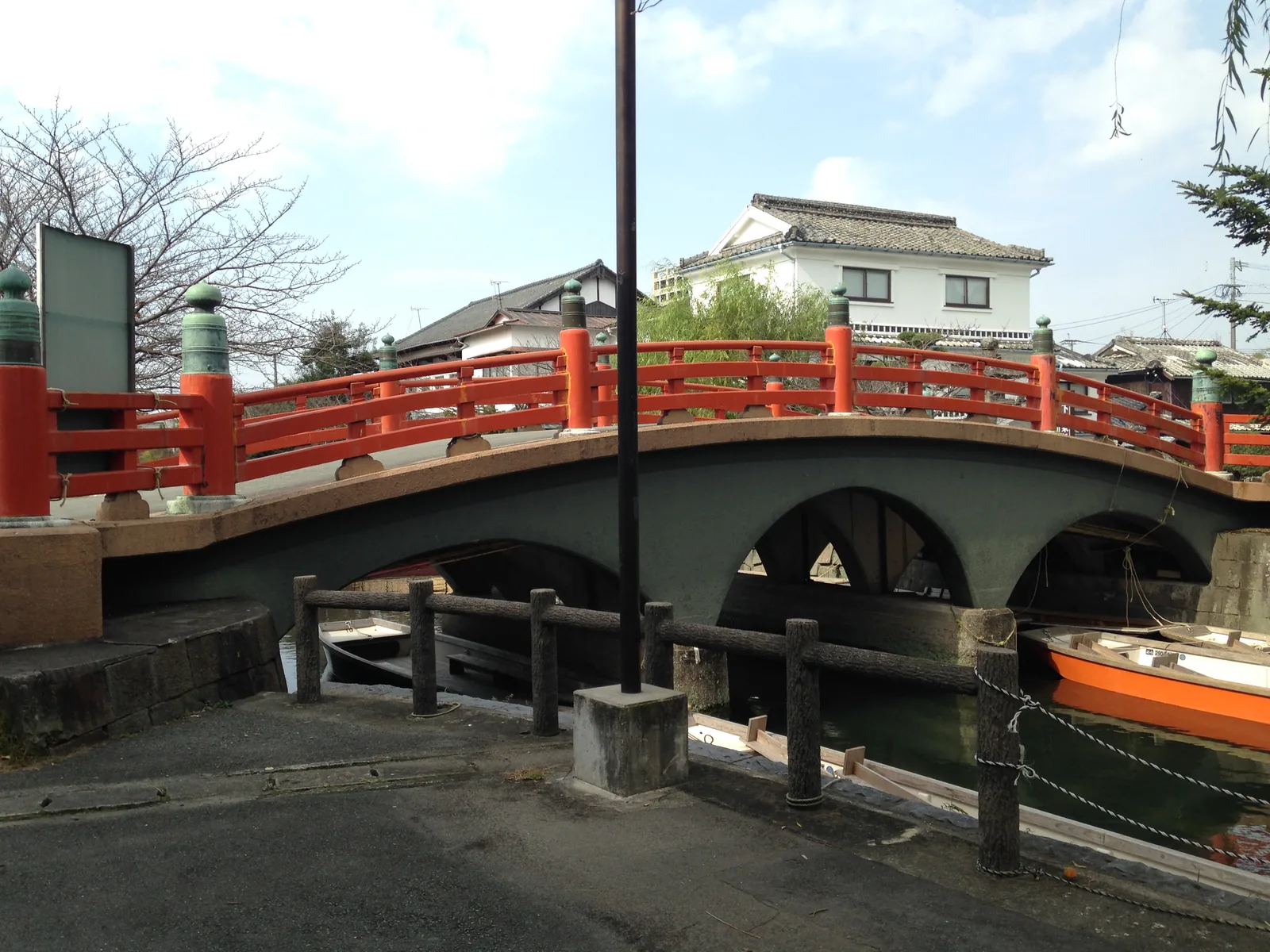 An arched bridge with red railings over the canal in front of Mihashira Shrine, with an orange boat moored below