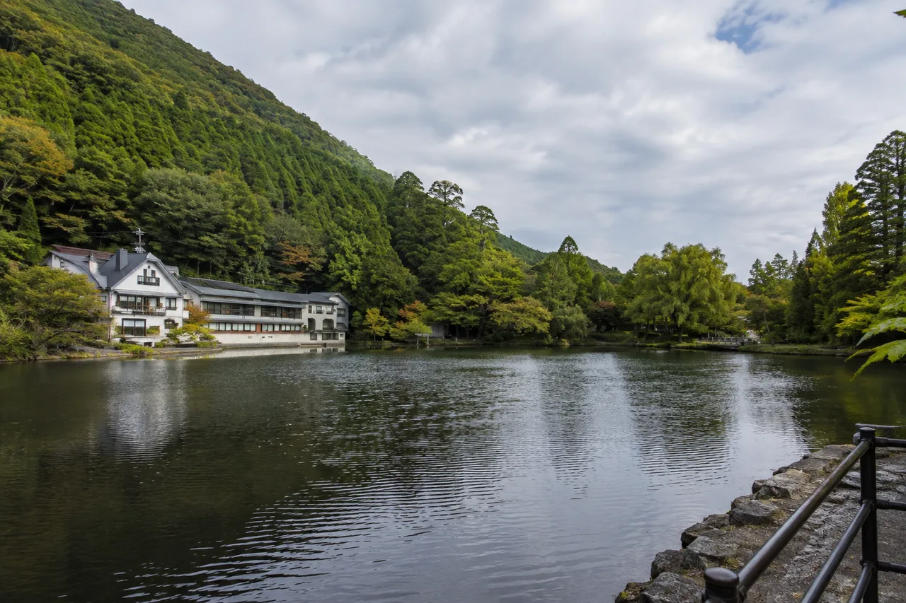 Lake Kinrin with a waterside building and wooded slope across the water, and a stone path railing at the right.